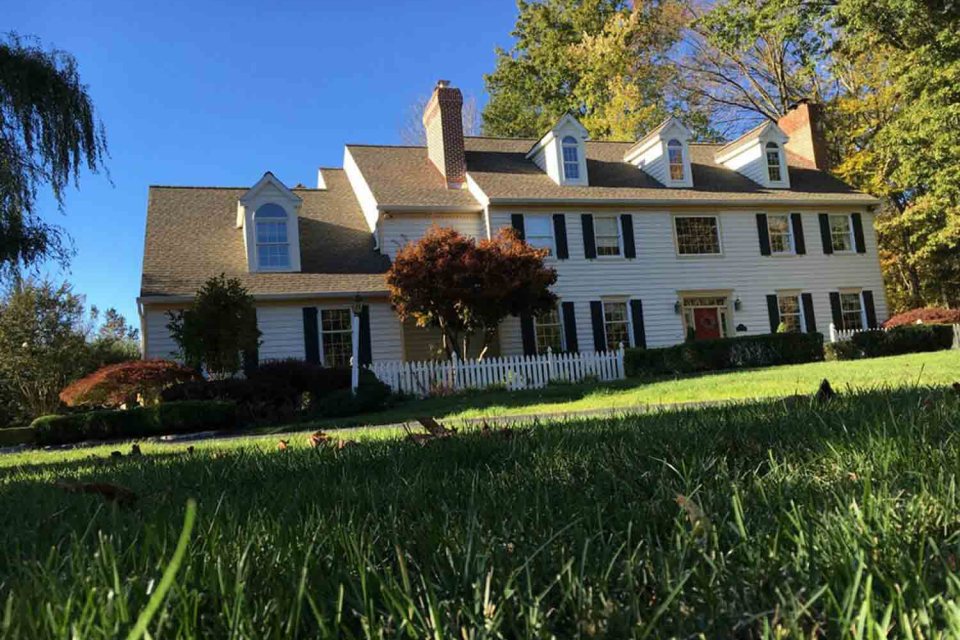 White colonial home with a dark shingle roof among autumn trees