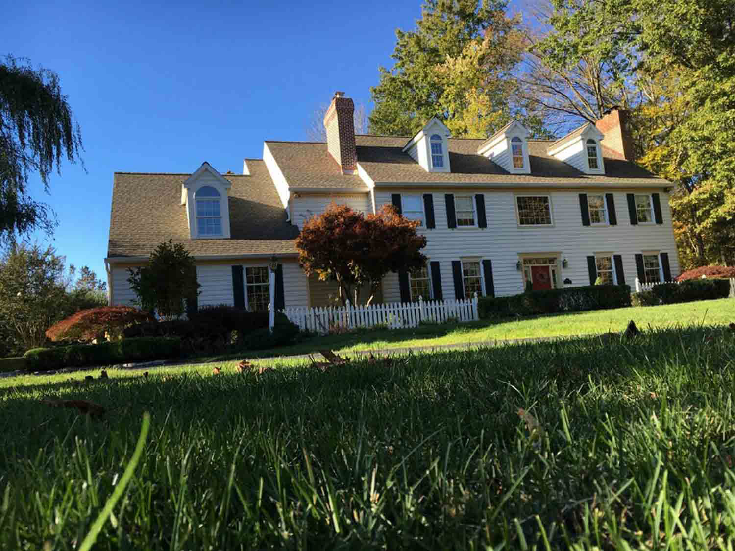 White colonial home with a dark shingle roof among autumn trees
