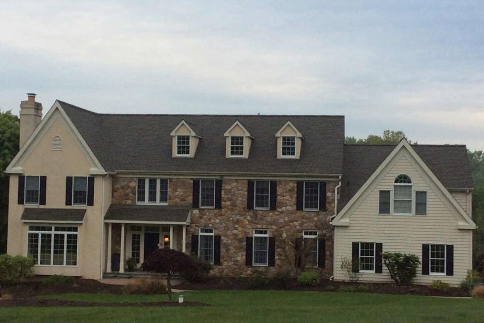 Shingle roof on a stone-and-stucco farmhouse with three dormers