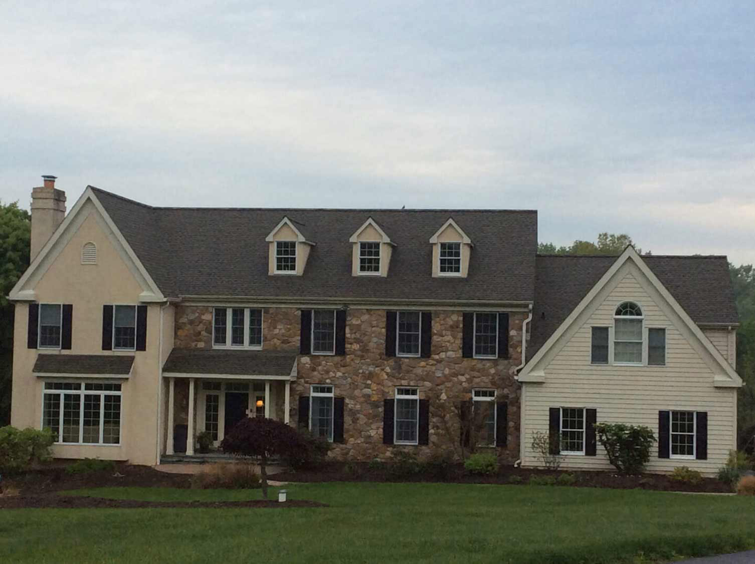 Shingle roof on a stone-and-stucco farmhouse with three dormers