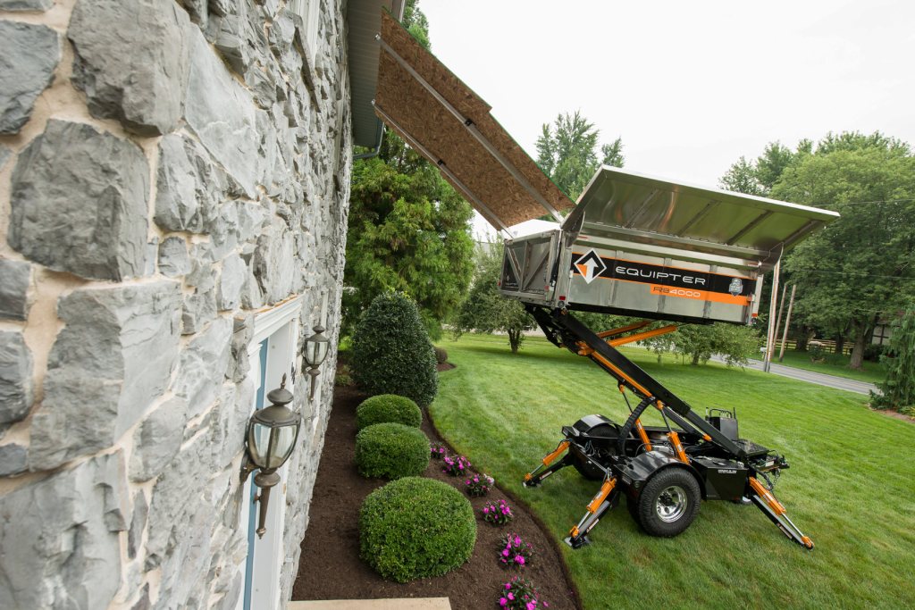 Debris trailer raised beside the stone wall of a house during roof work