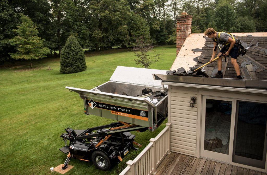 Roofer working at the roof edge above a debris trailer