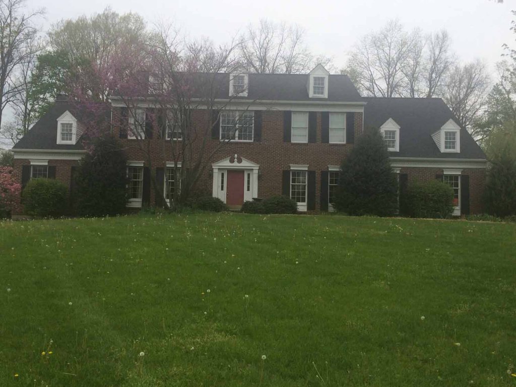 Shingle roof on a two-story brick colonial beyond a wide lawn