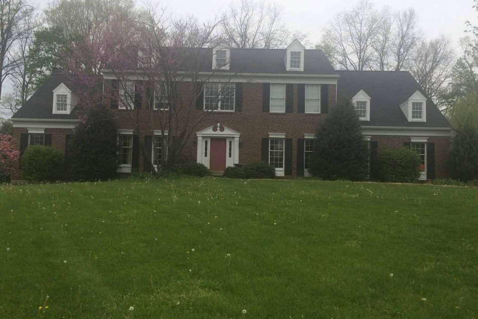 Shingle roof on a two-story brick colonial beyond a wide lawn