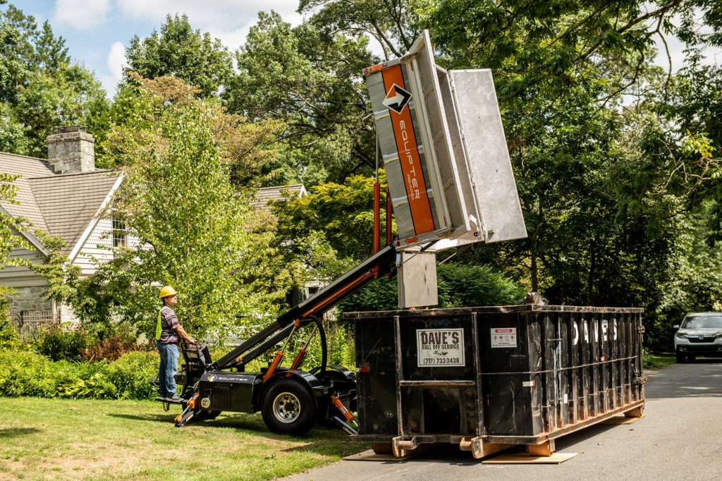 Debris trailer emptying into a dumpster in a driveway
