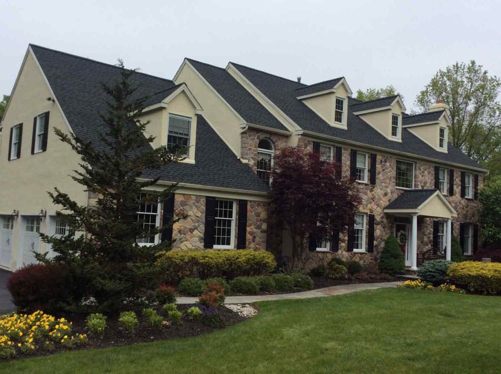 Shingle roof on a large stone-and-cream colonial with several dormers