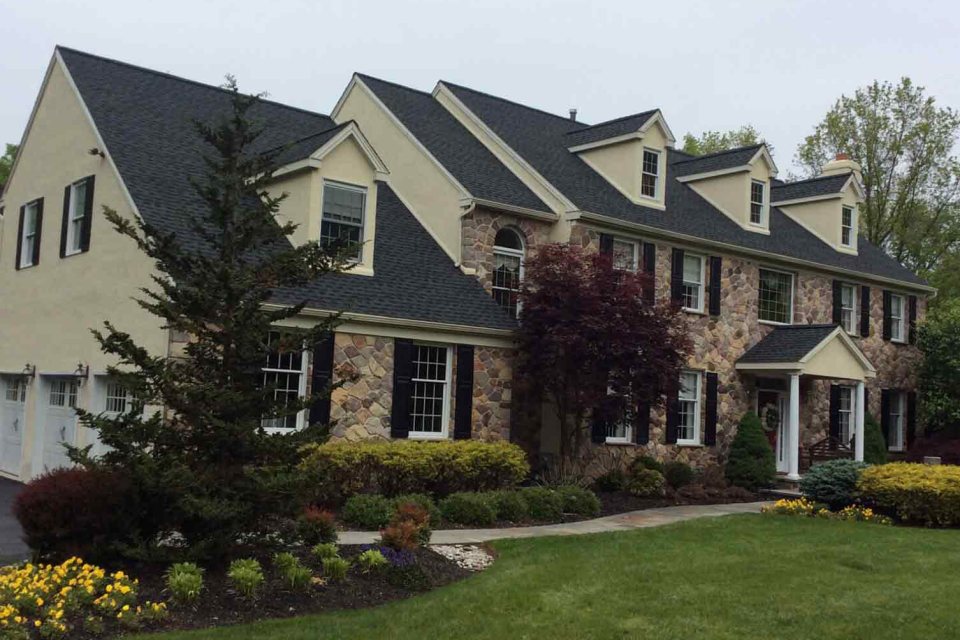 Shingle roof on a large stone-and-cream colonial with several dormers