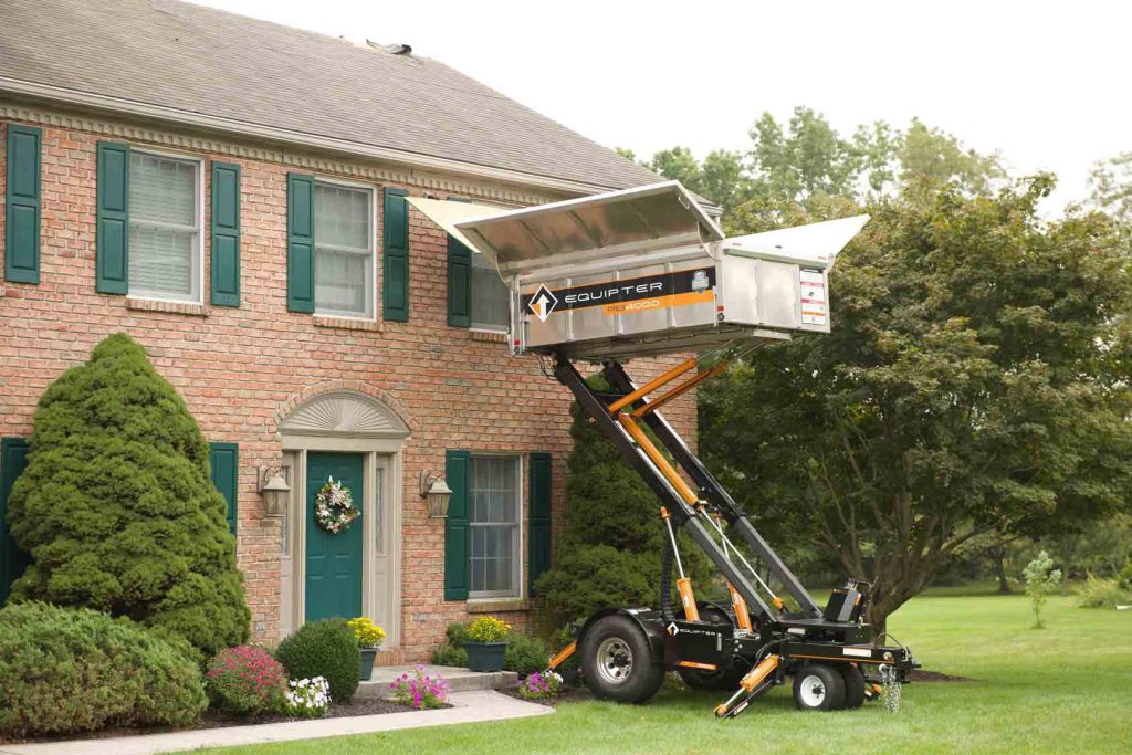 Debris trailer raised beside a brick house during a roof replacement